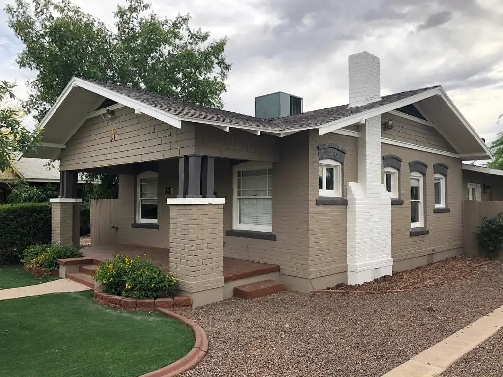 Angled view of the finished heritage bungalow showing taupe brick, white corner details, dark trim, and a landscaped walk.
