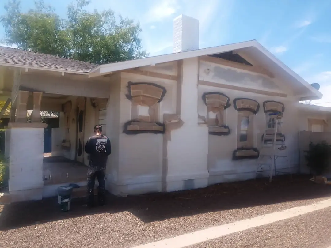 Painter working on the primed heritage facade, with window trim masked and a ladder beside the wall.